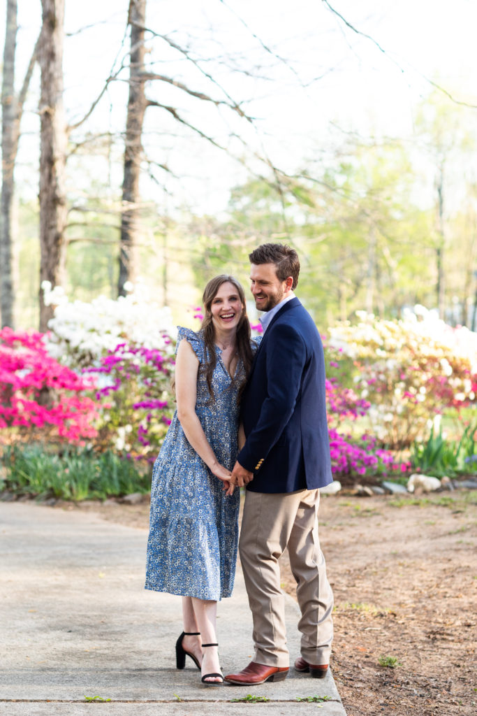 couple holding hands laughing together in front of flowers
